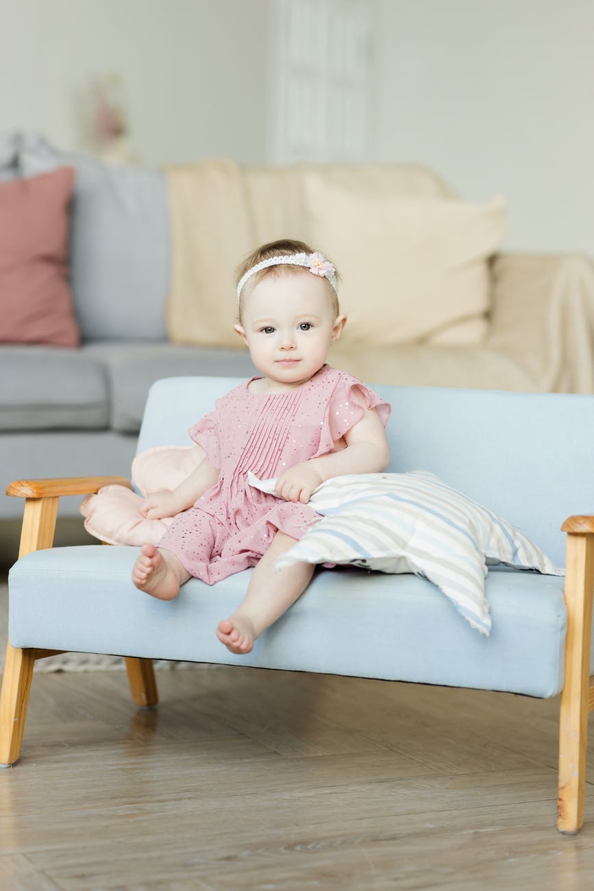 baby girl in pink dress sitting on sofa